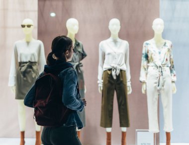 Kız dükkanın önünde duruyor ve mankenlerin üzerindeki kadın kıyafetlerine bakıyor..