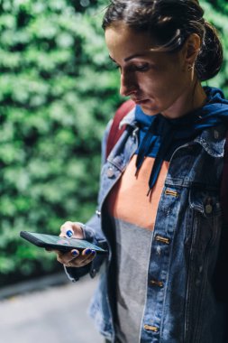 Kadın elinde bir akıllı telefon tutuyor ve ekrana bakıyor.