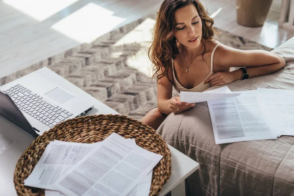 Femme travaille à la maison avec des documents. Les papiers sont étalés sur le lit — Photo