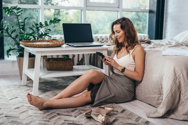 Wanita duduk di lantai dan melihat layar smartphone — Stok Foto