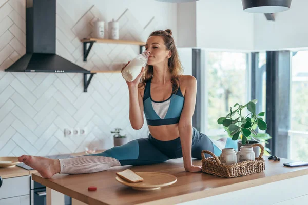 Passar kvinna som äter frukost i delad position på köksbordet. — Stockfoto