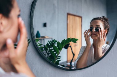 Genç bir kadın gözlerinin altına bantlar yapıştırıyor..