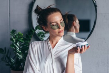 Kadın gözlerinin altına bant yapıştırıp banyoda duruyor.