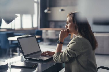 Takım elbiseli bir iş kadını ofisteki masasında dizüstü bilgisayarla çalışıyor.