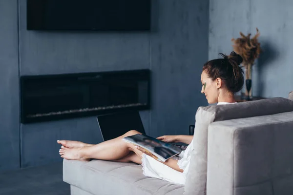 Femme à la maison regardant à travers un magazine brillant avec un verre lors d'une procédure de rajeunissement — Photo