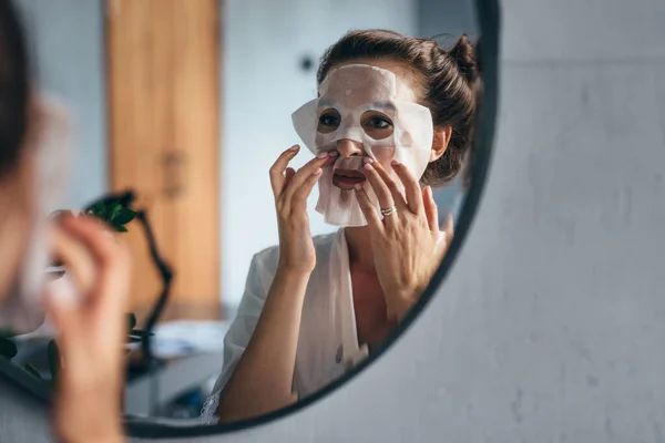 Cuidados com a pele. Uma mulher aplica uma máscara de lençol no rosto — Fotografia de Stock