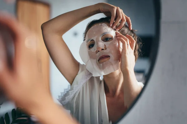 Mujer aplica mascarilla de sábana en su cara en el baño —  Fotos de Stock