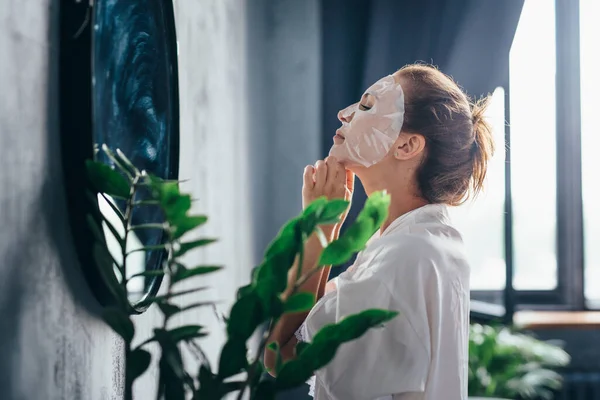 Mujer en el baño cuidando su piel facial mediante la aplicación de una máscara en su cara —  Fotos de Stock