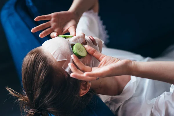 Femme couchée sur un canapé avec un masque de drap sur le visage et des tranches de concombre — Photo