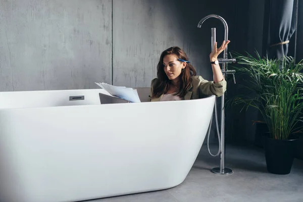 Žena na samotce v koupelně pracovat a sedí ve vaně s papíry — Stock fotografie