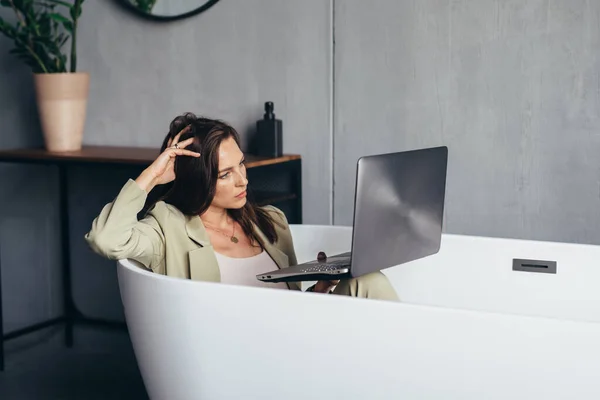 Mulher trabalha na banheira com seu laptop na privacidade de sua casa — Fotografia de Stock