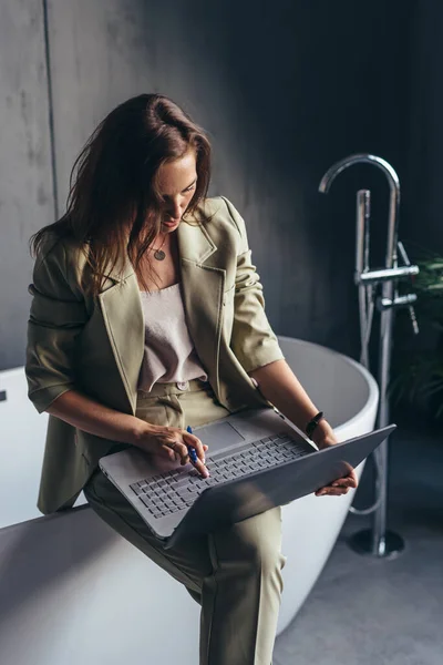 Žena schovává doma v koupelně se svým notebookem do práce. — Stock fotografie