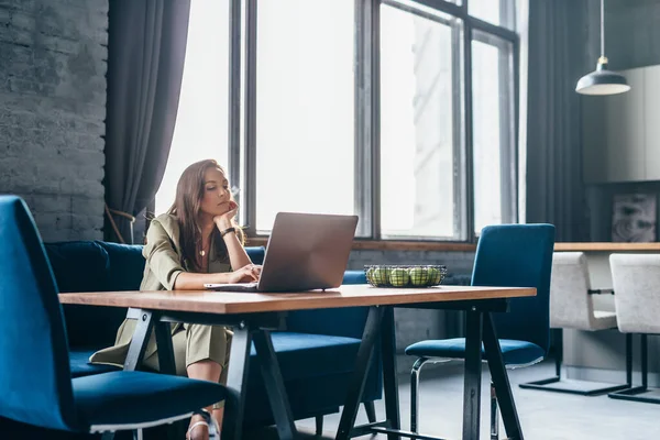 Žena doma sedí u stolu a dívá se na monitor notebooku — Stock fotografie