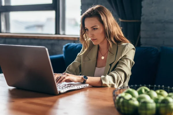 Kvinna hemma sitter vid skrivbordet med bärbar dator — Stockfoto