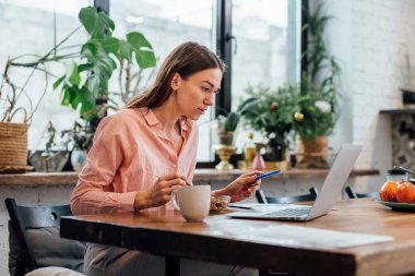 Genç bir kadın evde laptopuyla kahvaltı yapıyor.