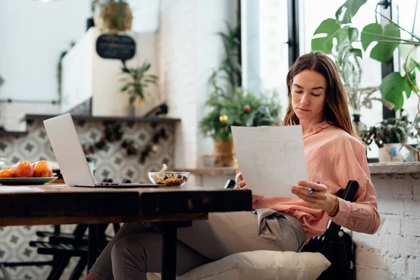 Mujer joven revisa documentos en la mesa de la cocina —  Fotos de Stock