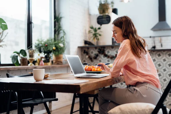 Jeune femme travaillant à la maison dans la cuisine avec un ordinateur portable. — Photo