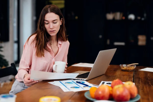 Mujer que trabaja en la oficina en casa sentada en el escritorio analizando estadísticas de negocios que contienen diagramas y gráficos usando computadora portátil. —  Fotos de Stock