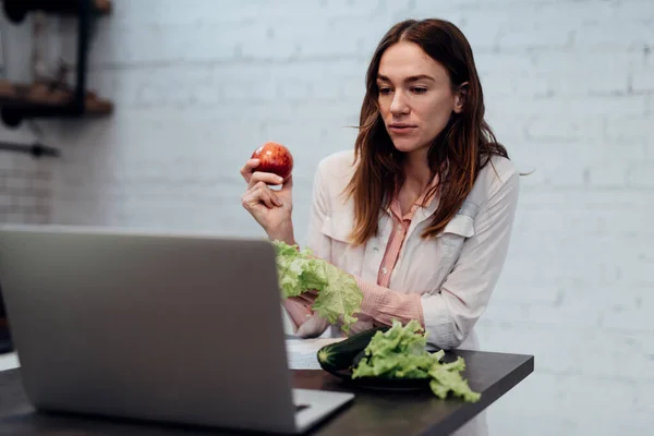 Doutor em dietética consulta online. Uma nutricionista feminina senta-se em sua mesa na frente de seu laptop e fala em uma chamada de vídeo ao vivo — Fotografia de Stock