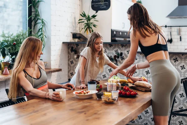 Las amigas y la hermanita hacen una comida ligera de verduras, frutas y ensaladas para un aperitivo después del entrenamiento.. —  Fotos de Stock