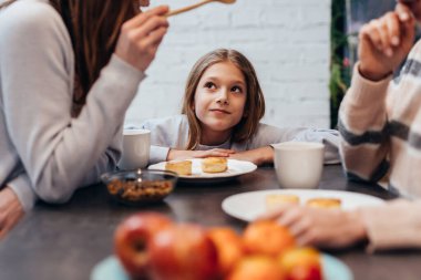 Kız, yetişkinlerin mutfak masasında konuştuklarını dinliyor..