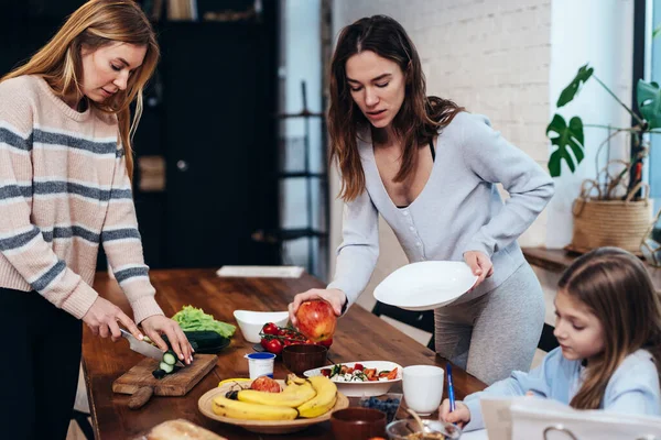 Las mujeres jóvenes ponen la mesa, la chica hace su tarea —  Fotos de Stock