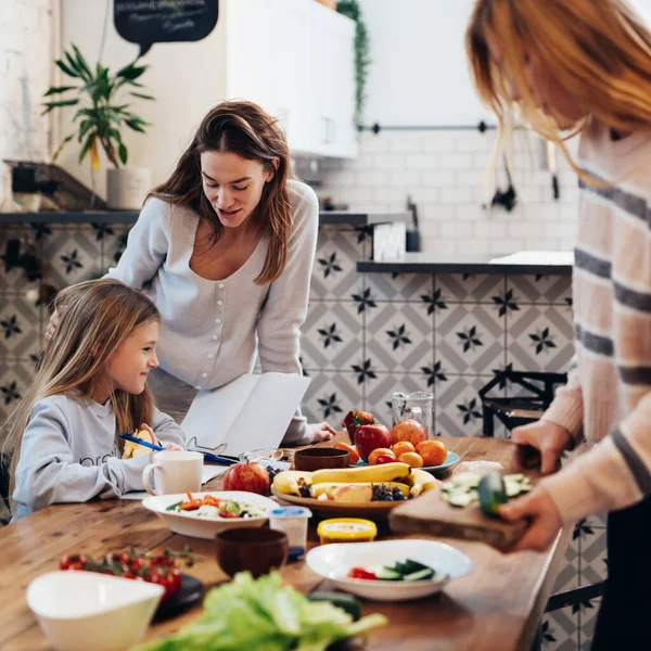 Preparándose para la cena familiar, las mujeres están poniendo la mesa, mientras que la niña está aprendiendo sus lecciones. — Foto de Stock