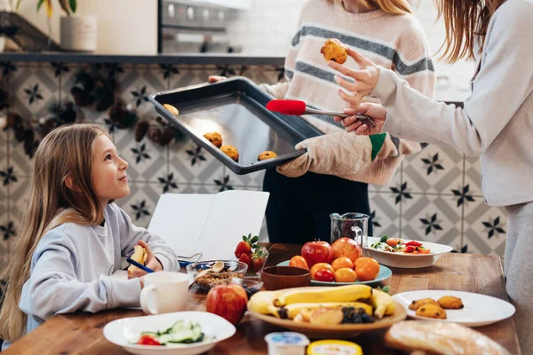Mädchen am Küchentisch erledigt ihre Hausaufgaben, während die Erwachsenen den Tisch zum Abendessen decken — Stockfoto
