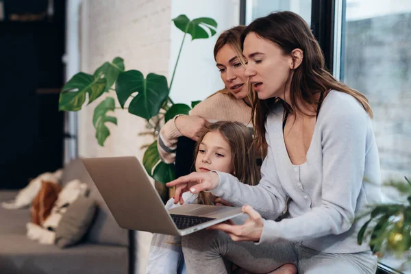 Amigas y una niña sentadas en casa en un alféizar viendo una película en un portátil. — Foto de Stock