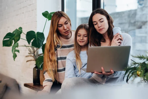 Las amigas y una niña están sentadas en casa en un alféizar viendo una serie. — Foto de Stock