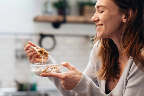 Ung kvinna hemma äter granola i köket — Stockfoto