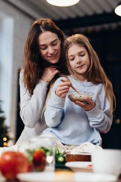 Vårdande, kramande mamma bredvid sin dotter äter granola — Stockfoto