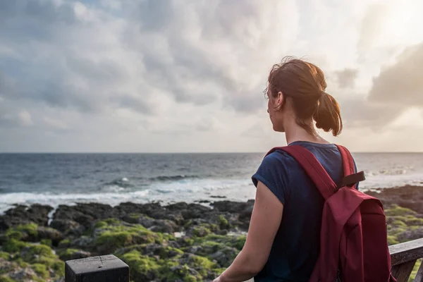 Jonge vrouw staat aan de kust en kijkt vooruit naar de zee — Stockfoto