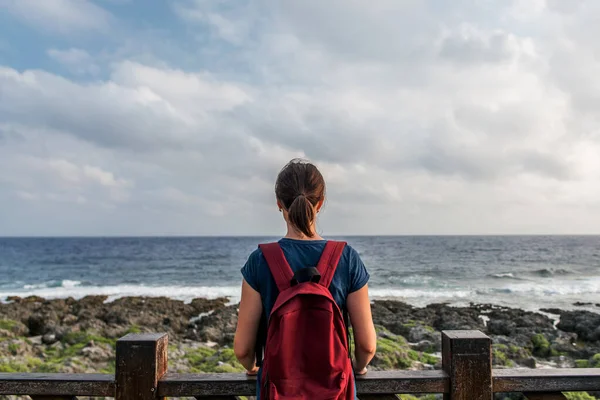 Jonge vrouw die aan zee staat en naar de horizon kijkt — Stockfoto