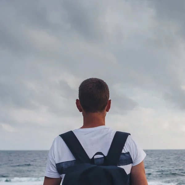 Giovane uomo in piedi vicino alla riva guardando il mare e il cielo. — Foto Stock