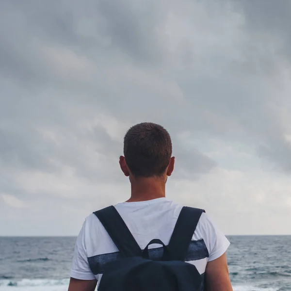 Joven parado junto a la orilla mirando el mar y el cielo. — Foto de Stock