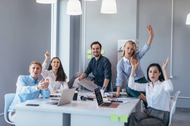 Bir grup genç iş adamı kameraya bakarken ellerini neşeyle sallıyorlar.