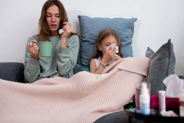 Madre e hija están enfermas juntas sentadas en el sofá debajo de la tela a cuadros. —  Fotos de Stock