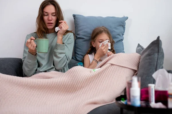 Madre e hija están enfermas juntas sentadas en el sofá debajo de la tela a cuadros. — Foto de Stock