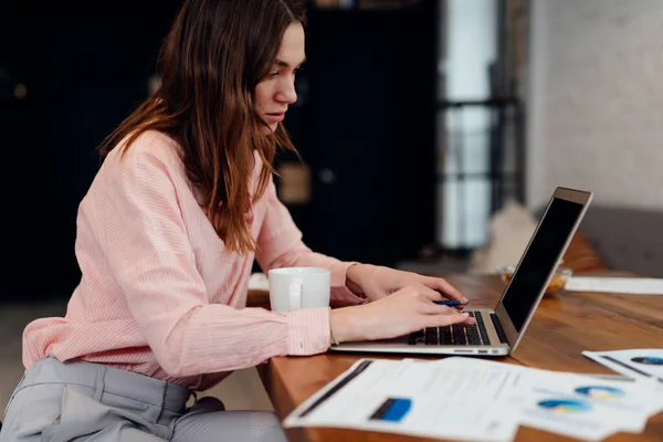 Mladá žena, pracující s dokumenty a notebook v kuchyni doma. — Stock fotografie