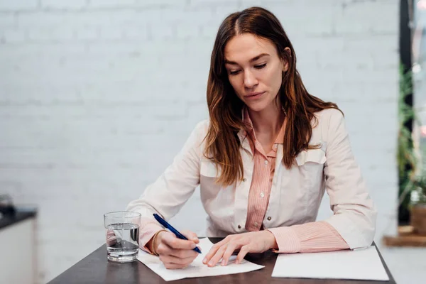 Женщина-врач сидит за своим столом и пишет ручкой на листе бумаги. — стоковое фото