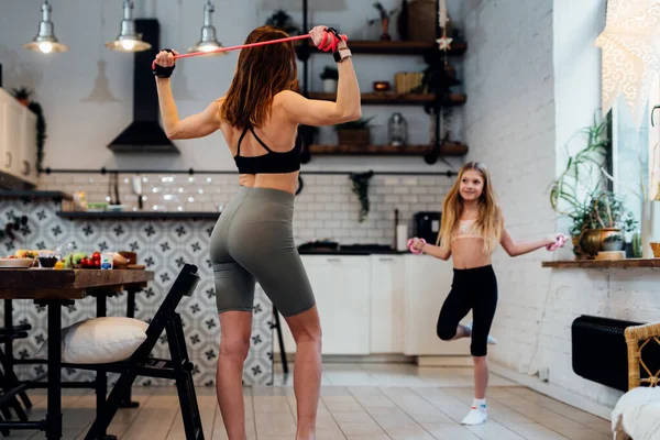 Joven madre haciendo ejercicio en casa con su hija. — Foto de Stock