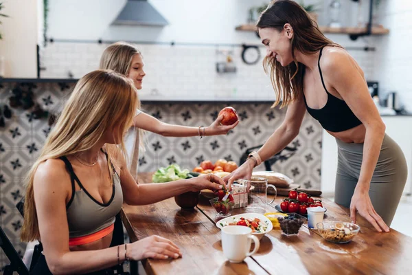 Mujer atlética prepara un aperitivo para su amigo y su hija después de un entrenamiento ligero en casa — Foto de Stock