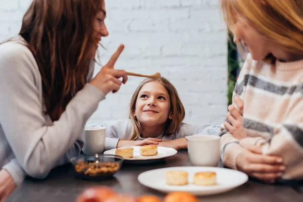 Female friends and a little girl sitting together at the table, eating and talking