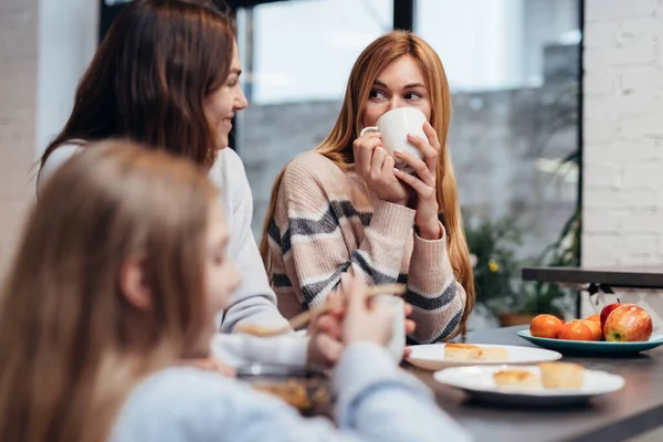 Freundinnen und ein kleines Mädchen sitzen zusammen am Küchentisch, trinken Kaffee und unterhalten sich. — Stockfoto