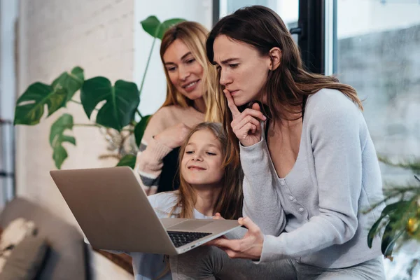 Las amigas y una niña se sientan juntas y miran la pantalla del portátil. — Foto de Stock