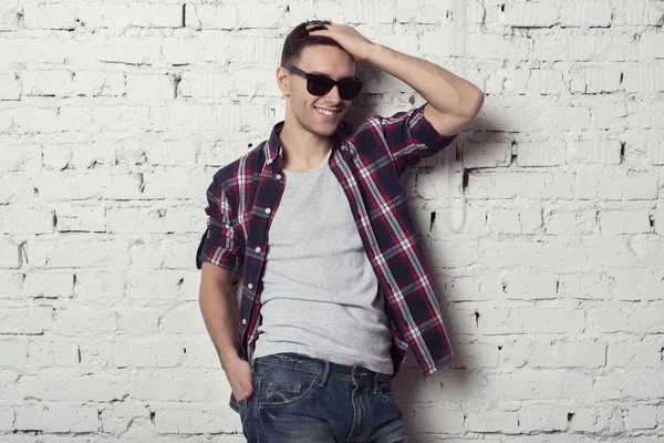 Jeune bel homme séduisant hipster avec des lunettes de soleil sa main dans les cheveux sourit — Photo