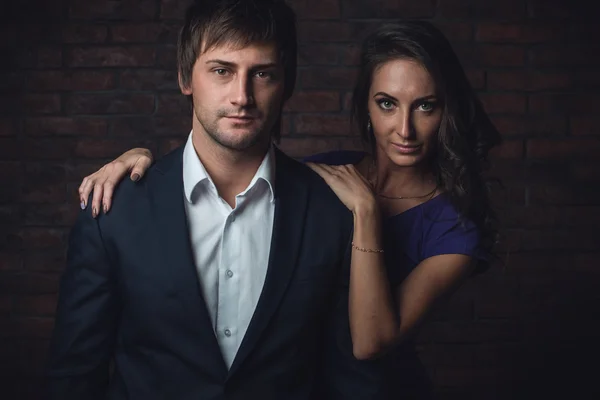 Feliz jovem casal apaixonado posando ao lado da parede vestidos elegantes . — Fotografia de Stock