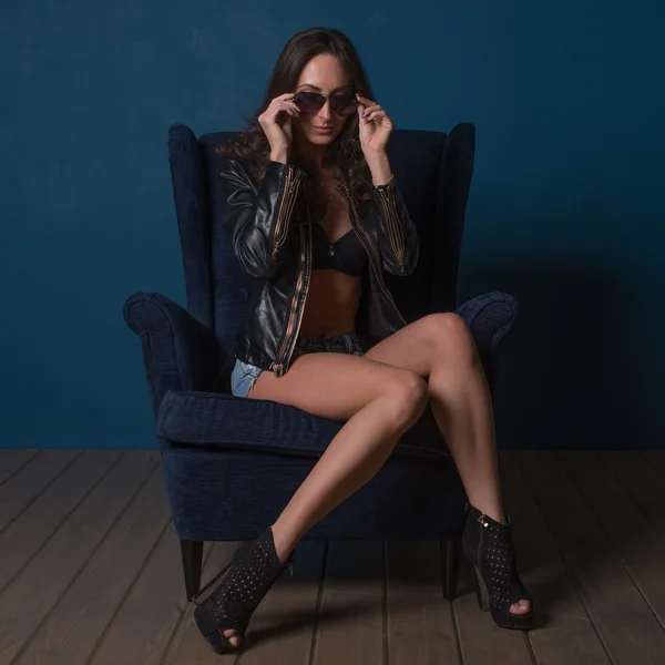 Young woman naked sexy legs at home sitting on modern armchair looking through sunglasses. — Stock Photo, Image