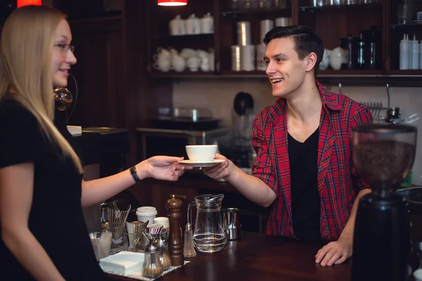 Hipster barista pasar orden taza de café o té con sonrisa a hermosa chica rubia —  Fotos de Stock